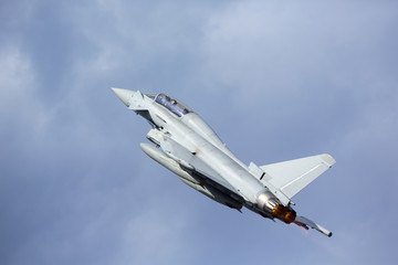 Modern tactical jet fighter flying close by and full throttle with afterburner glowing orange.