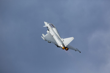 Modern tactical jet fighter flying close by and full throttle with afterburner glowing orange.