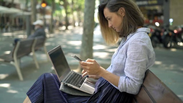 Businesswoman working with smartphone and laptop sitting in cafe in city

