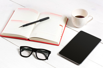 Office table desk with set of supplies, white blank notepad, cup, pen, tablet, glasses on white background. Top view