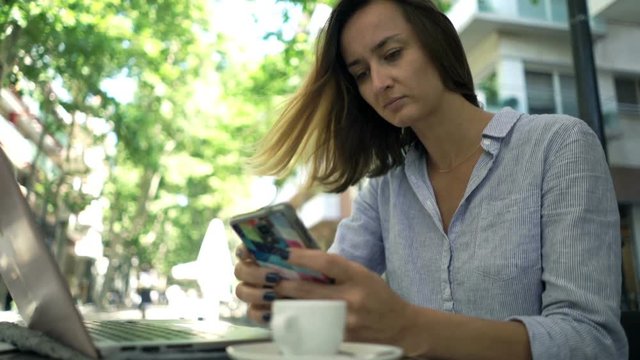 Businesswoman working with smartphone and laptop sitting in cafe in city

