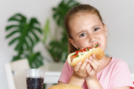 Young Cute European Girl In T-shirt Is Eating Unhealthy Food Like Hot Dog And Chips