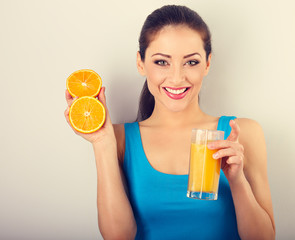 Beautiful toothy smiling fit young healthy casual woman holding the glass with orange juice and oranges in the hands. closeup toned portrait