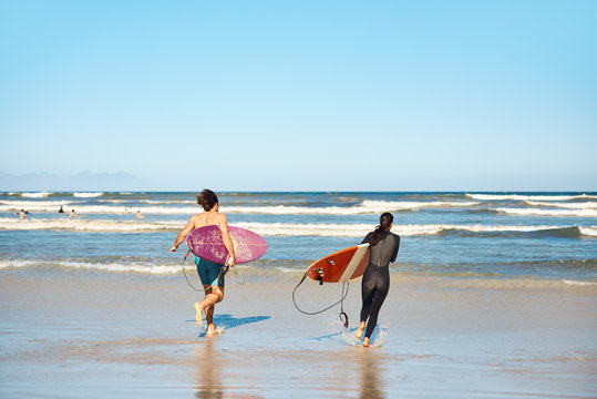 Friends couple walking into ocean with surfboards