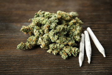 Heap of weed buds and cigarettes on wooden background