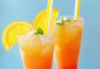 Glasses of Tequila Sunrise cocktail with orange slices on blue background, closeup