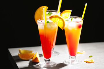 Glasses of Tequila Sunrise cocktail with orange slices on dark background