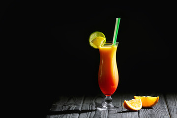 Glass of Tequila Sunrise cocktail with citrus slices on wooden table