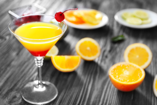 Glass of Tequila Sunrise cocktail with orange slices on wooden table