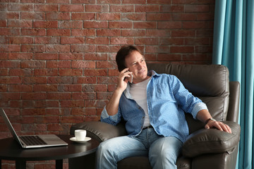 Mature man talking on phone while sitting in armchair