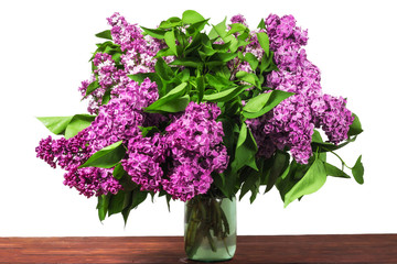 A bouquet of lilac flowers in a glass vase on a wooden table. On a white background.