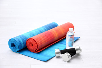 Two yoga mats with dumbbells and bottle of water on wooden floor
