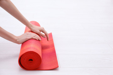 Woman rolling up yoga mat on wooden floor