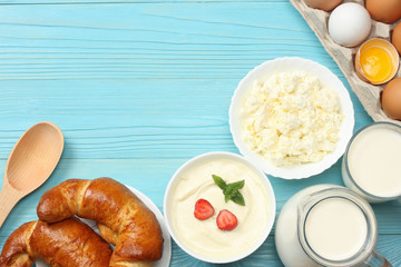 Milk background. Glass jug pitcher of fresh milk with glass, sour cream, cottage cheese, croissant and eggs on blue wooden background. Top view with copy space.
