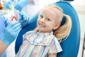 Dentist examining little girl's teeth in clinic
