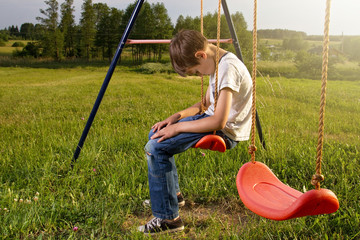 Sad lonely boy sitting on swing