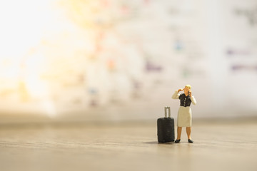 Travel concept. Female traveler miniature figures with black luggage calling mobile phone and...