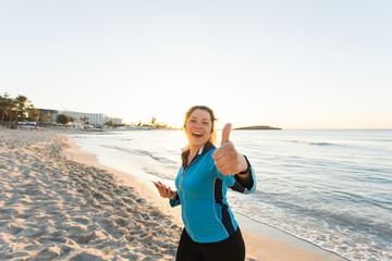 Fototapeta na wymiar Outdoor sport, fitness gadget and people concept - Smiling female fitness show thumbs up and holding smartphone with earphones.