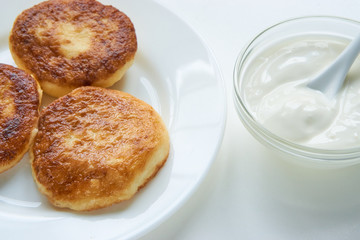 three pancakes on a white plate on white table with whipping sour cream. low angle close up shot. isolated white on white