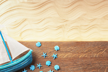 Composition with wooden board, small ship, sea shells and starfish on sand. Concept of travel and vacation