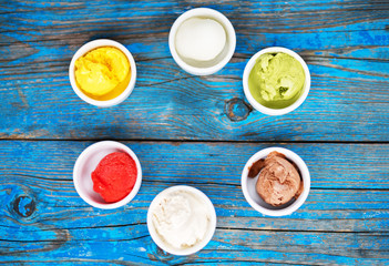 Selection of gourmet flavours of Italian ice cream in vibrant colors served in individual porcelain cups on an old rustic wooden table in an ice cream parlor.