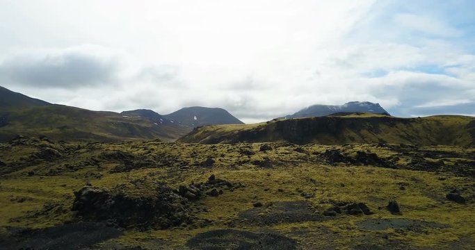 Aerial view of the lava field in Iceland. Copter flying over the green mountains with moss in cloudy day.