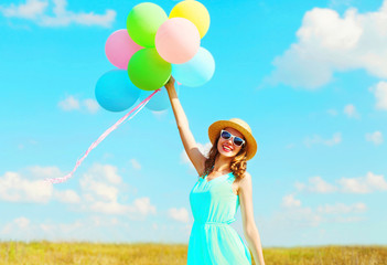 Happy young smiling woman holds an air colorful balloons at summer day over meadow blue sky