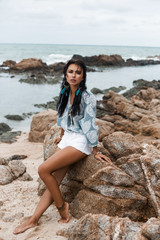 Fototapeta na wymiar Portrait of a beautiful, amazing dreamy girl, against the sea, perfect face, brooding look, bronze skin, dark long hair, shirt, accessories, feather earrings, indie, bohemian, Bo-ho style, summer
