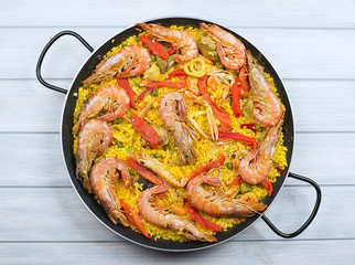 From above big paella dish containing shrimps and rice with vegetables.