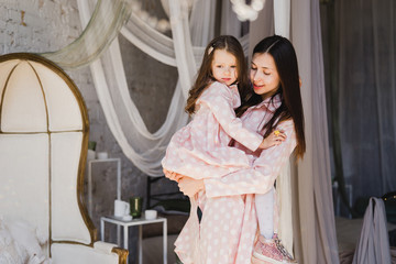 Mother and daughter hugging and playing together. Pretty little girl on beautiful woman's lap. Girls in pink dresses playing in decorated room. Family weekend, beauty day, having fun, love concept.