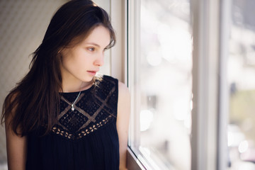 Photo of young beautiful woman with long hair near the window. Sunny day. City lifestyle.