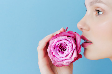Portrait of a beautiful brunette girl with a pink rose on a blue background