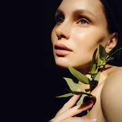 Portrait of a beautiful young brunette woman with green leaf in his hand in the studio, the concept of beauty and health