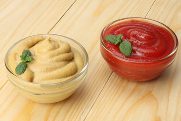 mustard ketchup in glass bowl on wooden background. © Tatiana