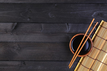Background for sushi. Bamboo mat and soy sauce on black wooden table. Top view with copy space