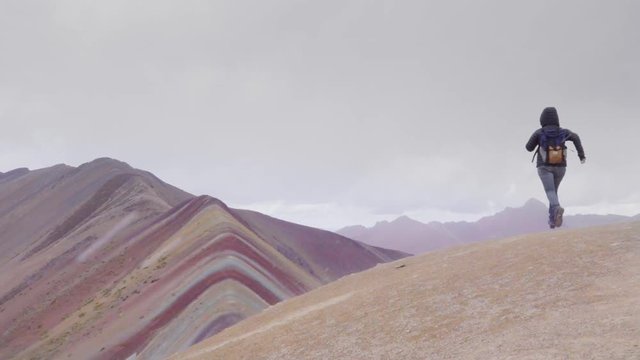 Woman walking on the top of a mountain, panoramic view of the Rainbow mountain in Peru. Slow motion 	