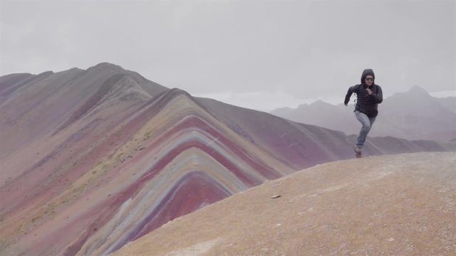 Woman runs on the top of a mountain, panoramic view of the Rainbow mountain in Peru. Slow motion 	