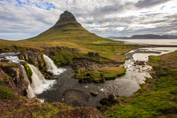 Summer cloudy day with Kirkjufell volcano on the coast of Snaefellsnes peninsula. Idyllic scene of Kirkjufellsfoss waterfall, Iceland,