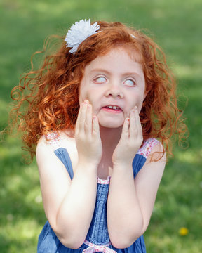 Portrait Of Cute Adorable Little Red-haired Caucasian Girl Child In Blue Dress Making Funny Scary Silly Faces In Park Outside, Child Rolling Eyes, Having Fun, Lifestyle Childhood Concept