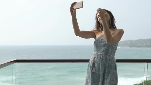 Young woman taking selfie photo with cellphone standing on terrace
