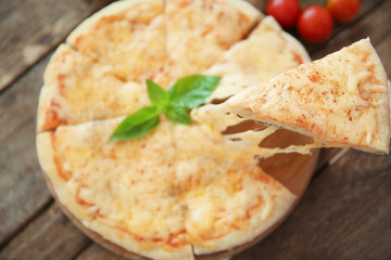 Tasty sliced pizza with basil leaves on wooden table
