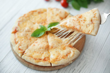 Tasty sliced pizza with basil leaves on wooden table