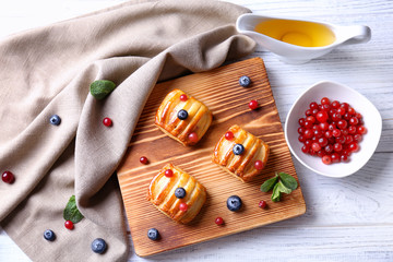 Wooden cutting board with pastries and berries on white table, top view