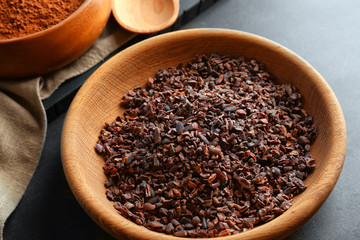 Cocoa nibs in wooden bowl on grey table
