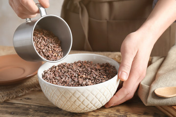 Person pouring cocoa nibs from cup into bowl on table