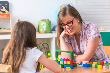 Preschool teacher with small girl in the classroom playing