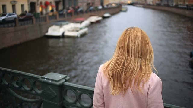A woman in a coat stands on a bridge and looks down at the black water. She wants to commit suicide