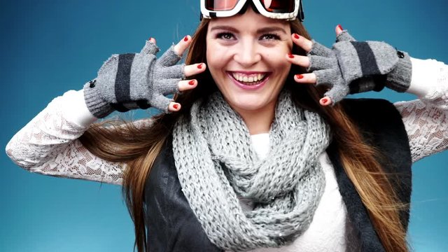 Woman smiling skier girl wearing warm clothing ski goggles showing red nails manicure. Winter sport activity. Beautiful long hair sportswoman on blue studio shot, full HD.