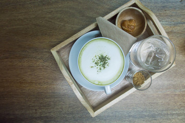Hot green tea latte with matcha powder on wooden background.
