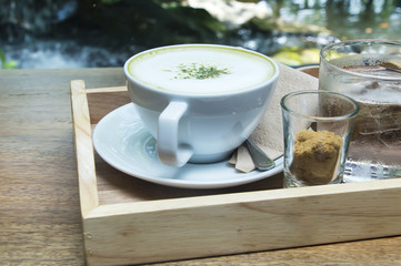 Hot green tea latte with matcha powder on wooden background.